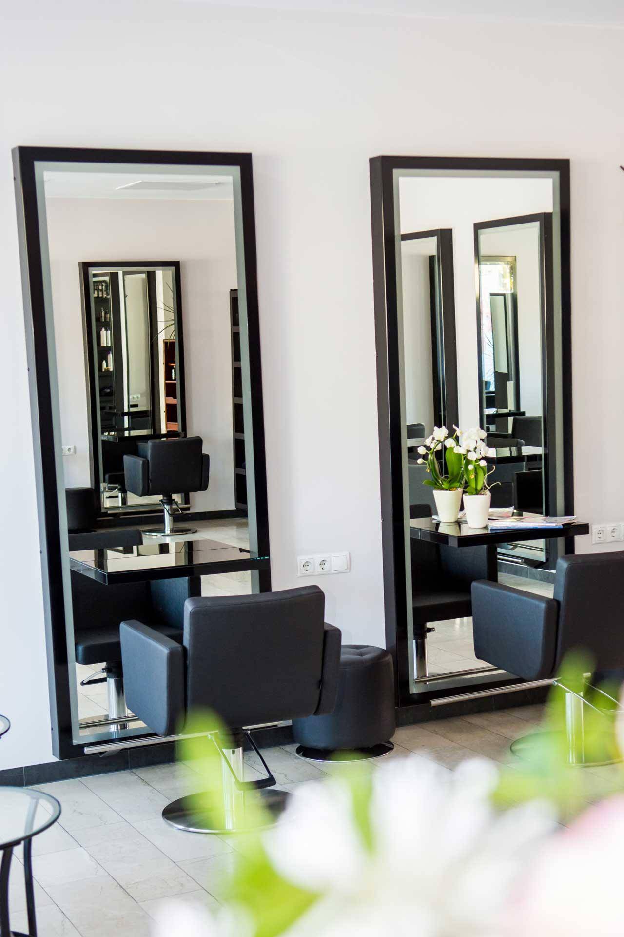 Heller Friseursalon mit großen Spiegeln, modernen Stühlen und hellem Holzfußboden.