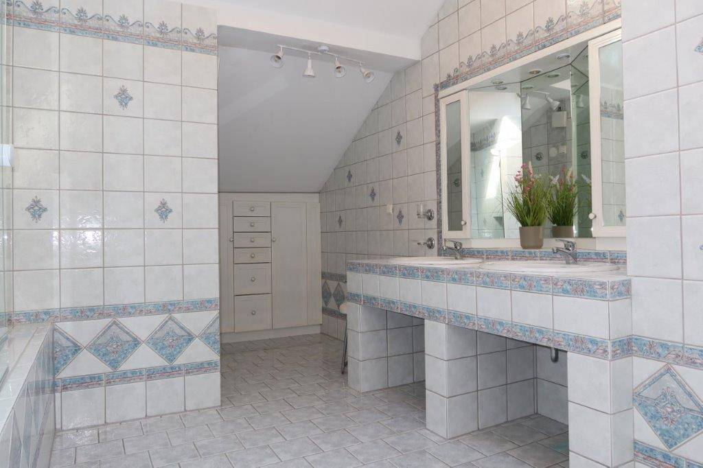 Badezimmer im Dachgeschoss mit Doppelwaschbecken und gefliesten Wänden in hellem Muster.