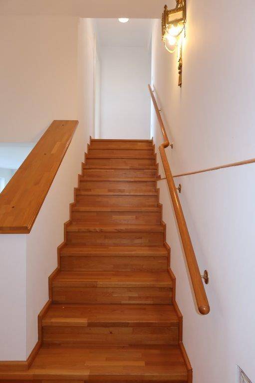 Holztreppe mit Handlauf, die in die obere Etage führt.
