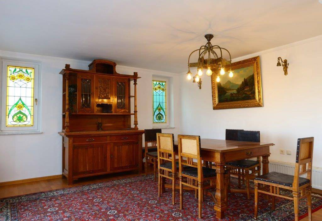 Traditioneller Essbereich mit Holztisch, antiker Anrichte und farbigen Glasfenstern.