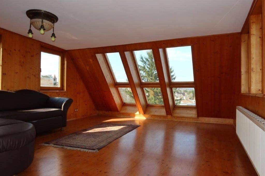 Wohnraum im Dachgeschoss mit Holzverkleidung, schrägen Fenstern und Holzboden.