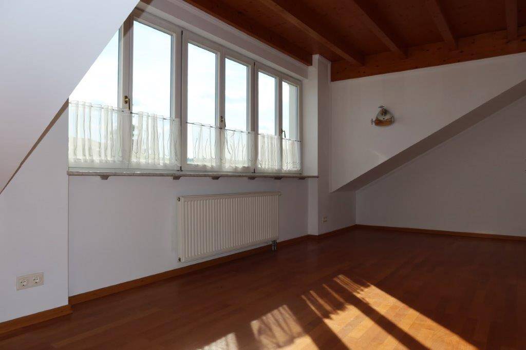 Leerer Raum im Dachgeschoss mit Holzbalkendecke und großen Fenstern.