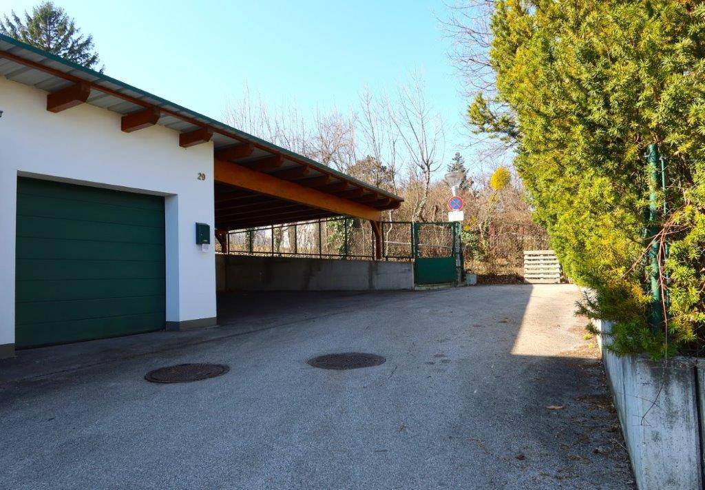 Einfahrt mit Garage und überdachtem Stellplatz für Fahrzeuge.