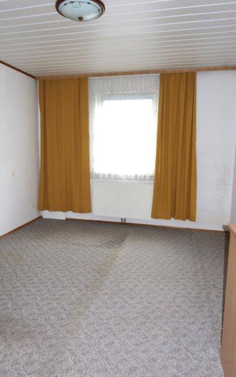 Leerer Raum mit gemustertem Teppichboden und gelben Vorhängen am Fenster.