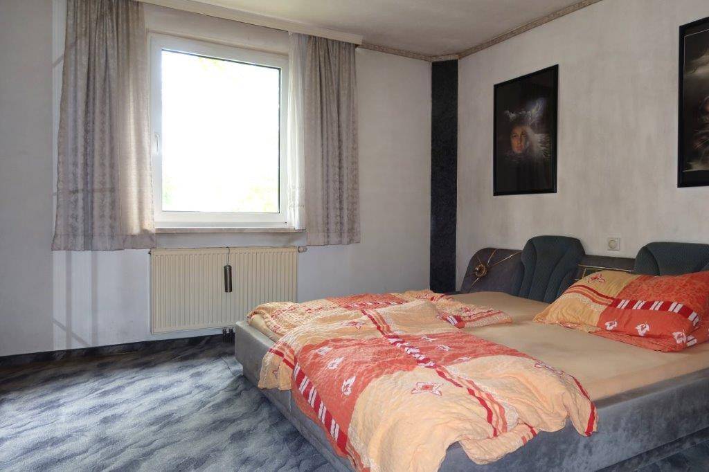 Schlafzimmer mit großem Bett, Fenster und dunklem, gemustertem Bodenbelag.