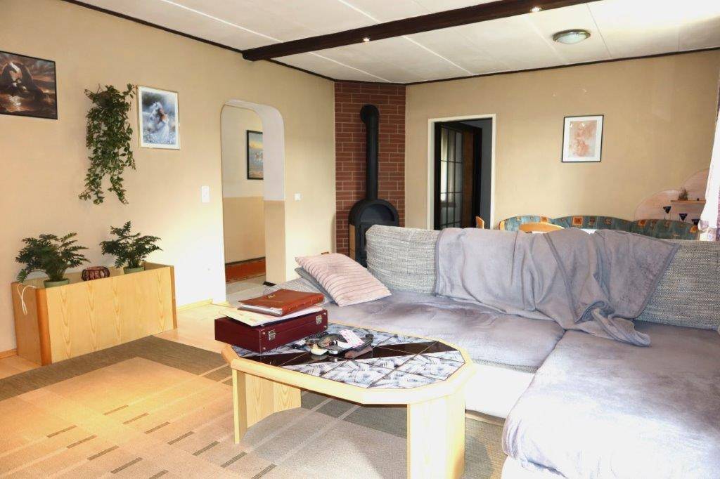 Helles Wohnzimmer mit gemütlichem Sofa, Kaminofen und Zugang zu weiteren Räumen.