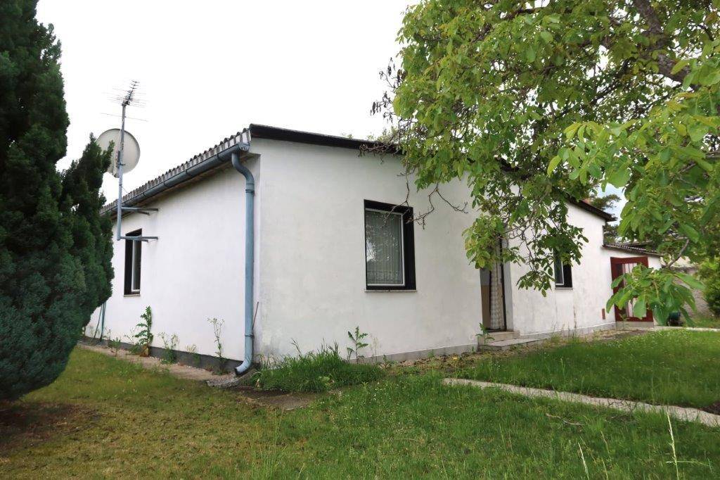 Seitenansicht des Hauses mit weißer Fassade, Gartenbereich und Bäumen.
