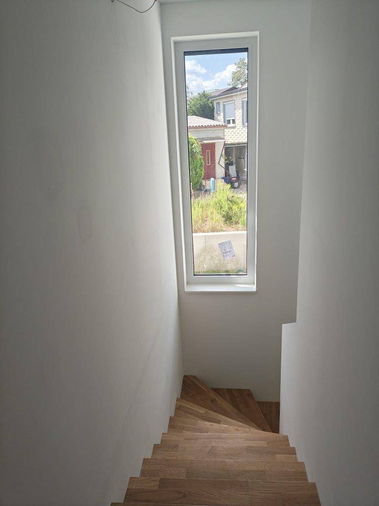Unmöblierter Treppenaufgang mit Holzstufen und hohem Fenster, das viel Tageslicht spendet.