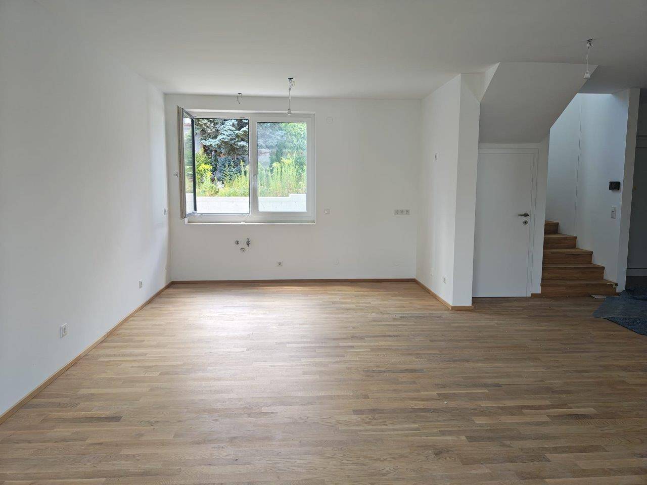 Leerer Küchenbereich mit Holzboden und Fenster, offen zum Treppenaufgang, bereit zur Installation.