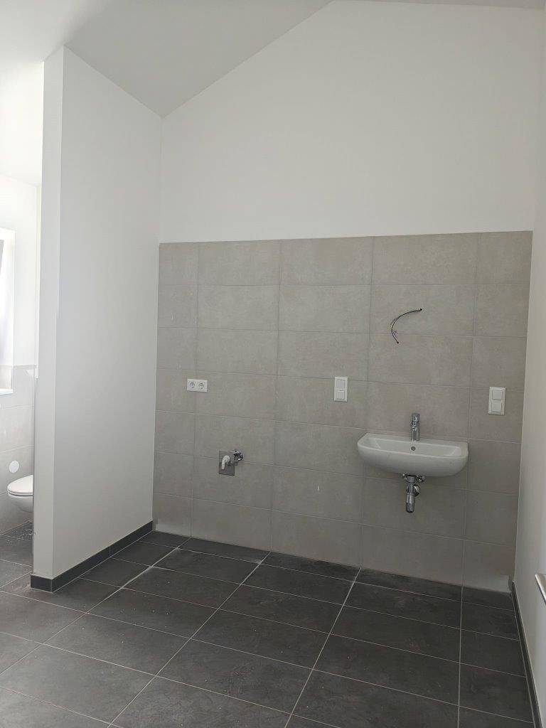 Unmöbliertes Badezimmer mit Fliesenboden, Waschbecken und Toilette, bereit zur individuellen Gestaltung.