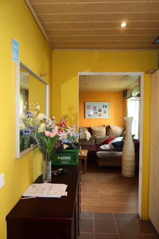 Heller Flur mit gelben Wänden, einem Spiegel und Blick in das angrenzende Wohnzimmer.