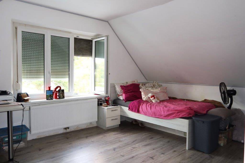 Gemütliches Schlafzimmer im Dachgeschoss mit schrägen Wänden, einem Bett und einem Fenster mit Rollläden.
