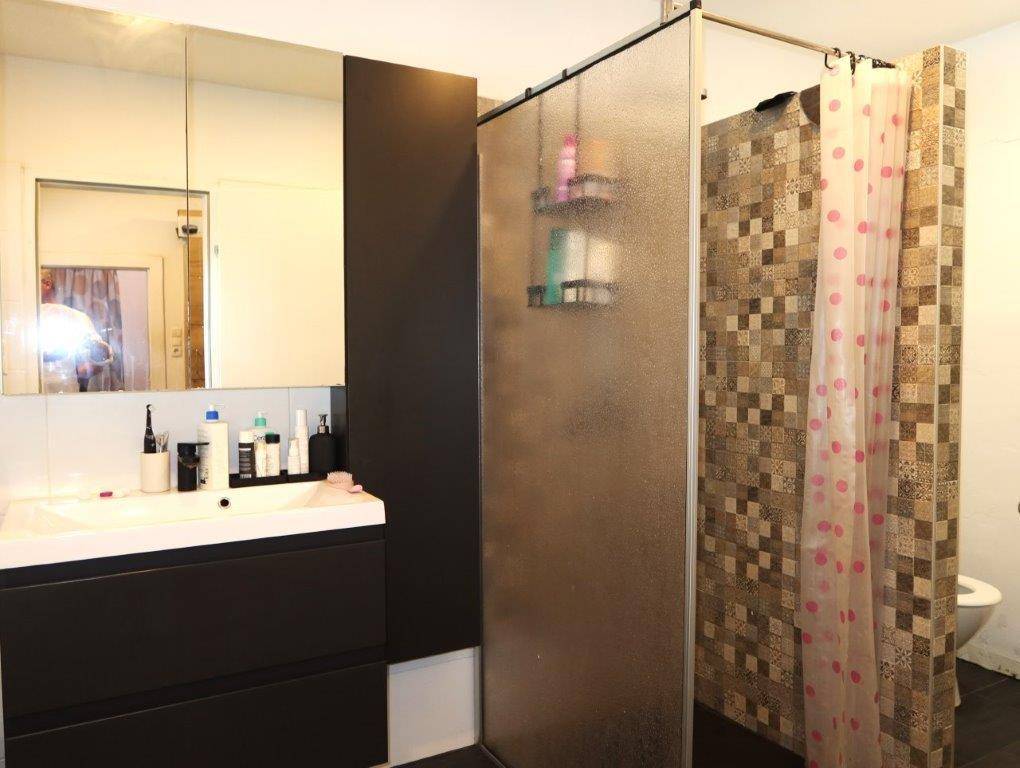 Modernes Badezimmer mit dunklem Waschtisch, Spiegel und einer Duschkabine mit gemusterten Fliesen.