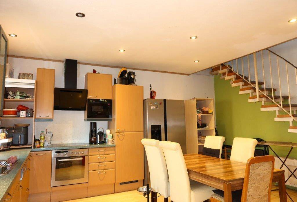 Funktionale Küche mit Holzelementen, Essbereich und offener Treppe in einem hellen Raum.