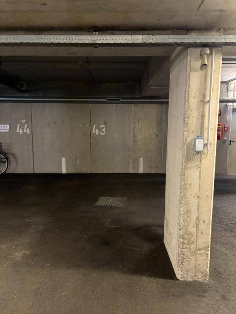 Tiefgarage mit nummerierten Stellplätzen, Betonwänden und freiliegenden Installationen an der Decke.
