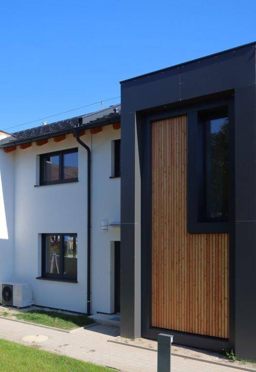 Moderne Hausfassade mit weißem Putz und dunklen Holzverkleidungen unter blauem Himmel.
