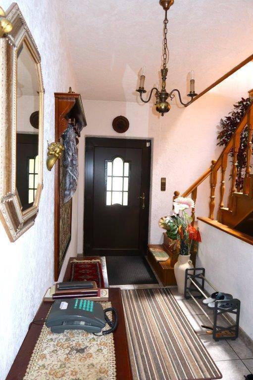 Traditioneller Eingangsbereich mit dunkler Holztür, Spiegel und einer eleganten Holztreppe.