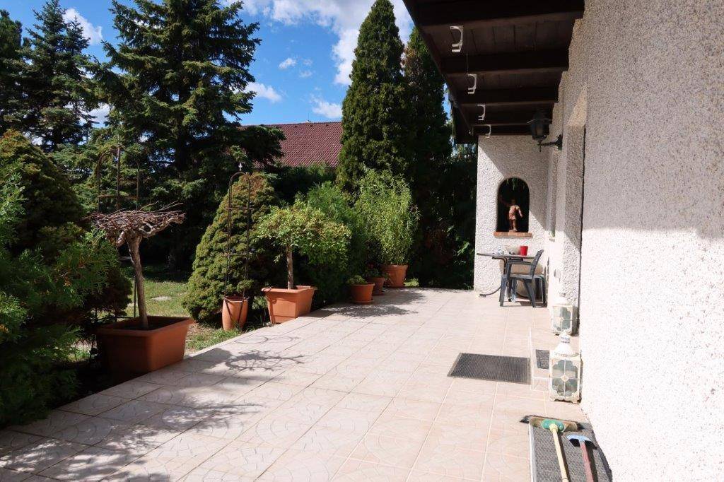 Große gepflasterte Terrasse mit Topfpflanzen und einem kleinen Sitzbereich neben dem Haus.
