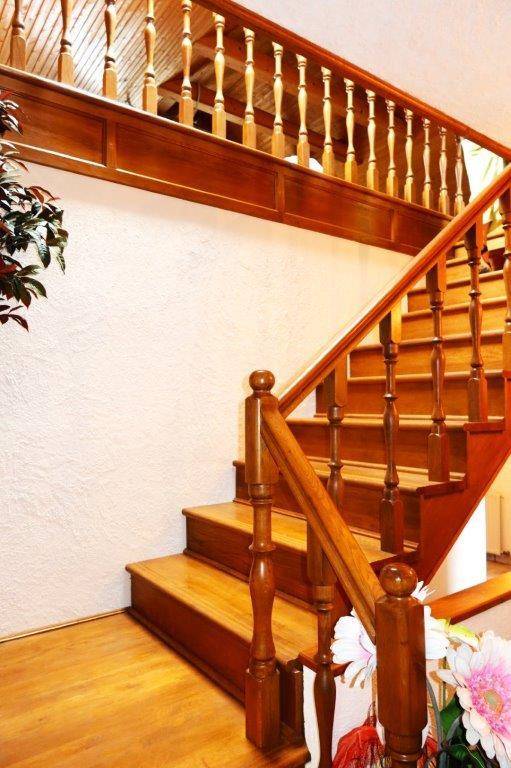 Detailaufnahme einer massiven Holztreppe mit kunstvoll gedrechselten Geländerstäben und Handlauf.