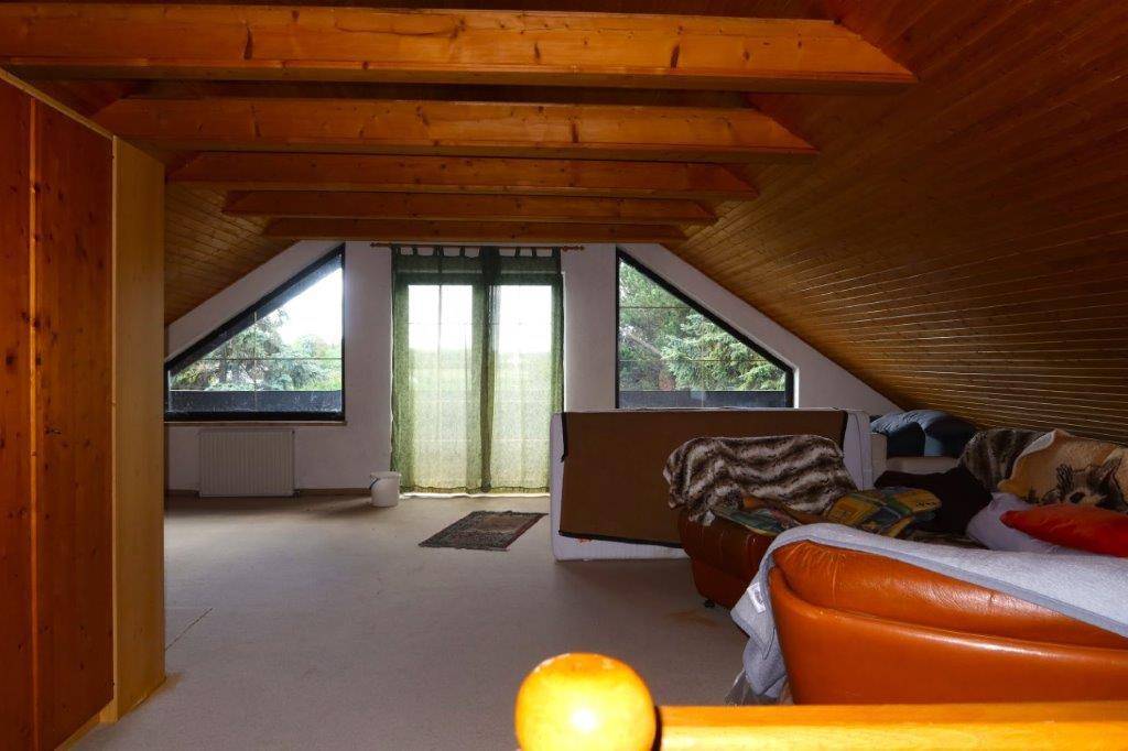 Ausgebautes Dachgeschoss mit sichtbaren Holzbalken, Holzverkleidung und dreieckigen Fenstern.