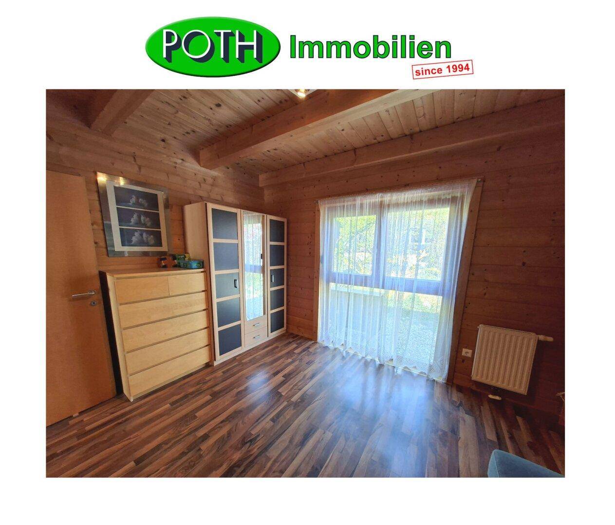 Helles Schlafzimmer mit Holzwänden, Laminatboden und großem Fenster mit Vorhängen.