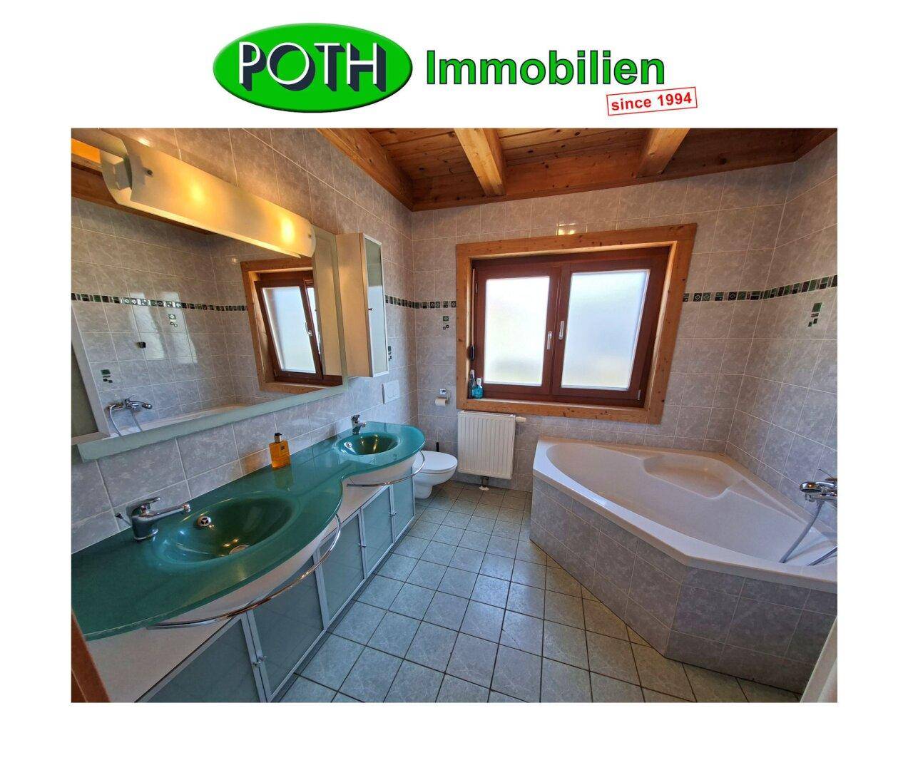 Badezimmer mit Doppelwaschbecken, Eckbadewanne und Fliesenboden in hellem Grau.