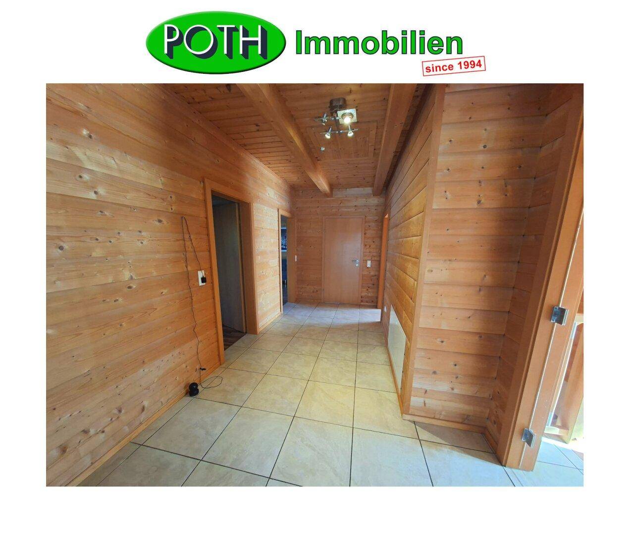 Heller Flur mit Holzvertäfelung an Wänden und Decke sowie hellem Fliesenboden.