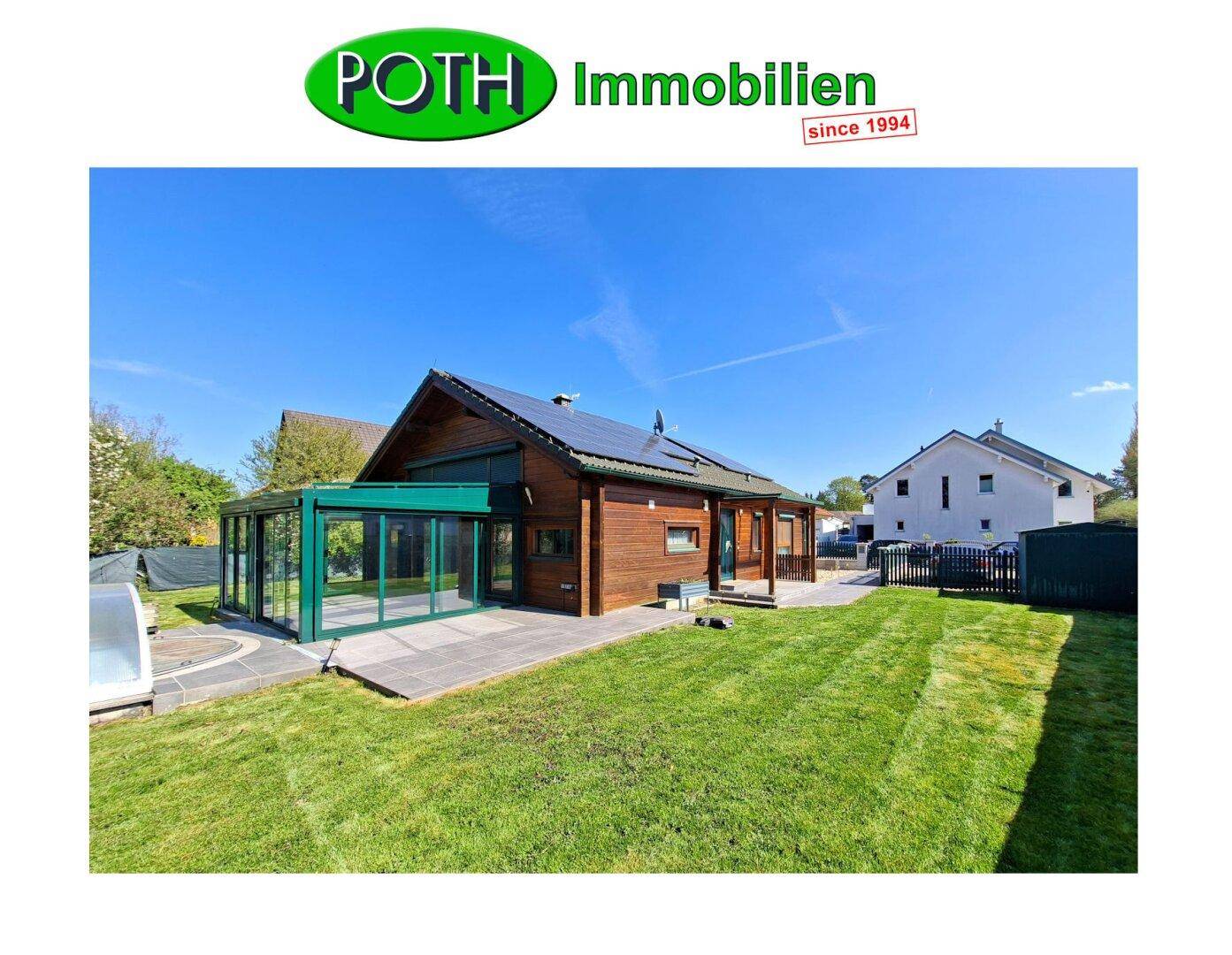 Blockhaus mit weitläufigem Garten, Pool und verglastem Anbau unter strahlendem Himmel.