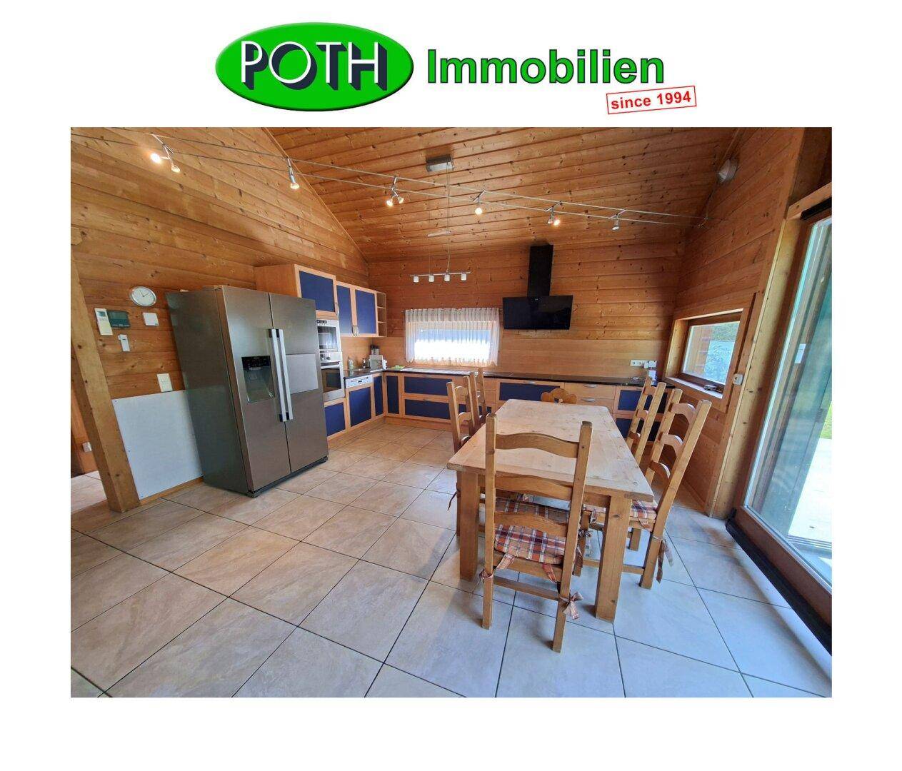 Rustikale Wohnküche mit Holzwänden, blauen Schränken und großem Esstisch.