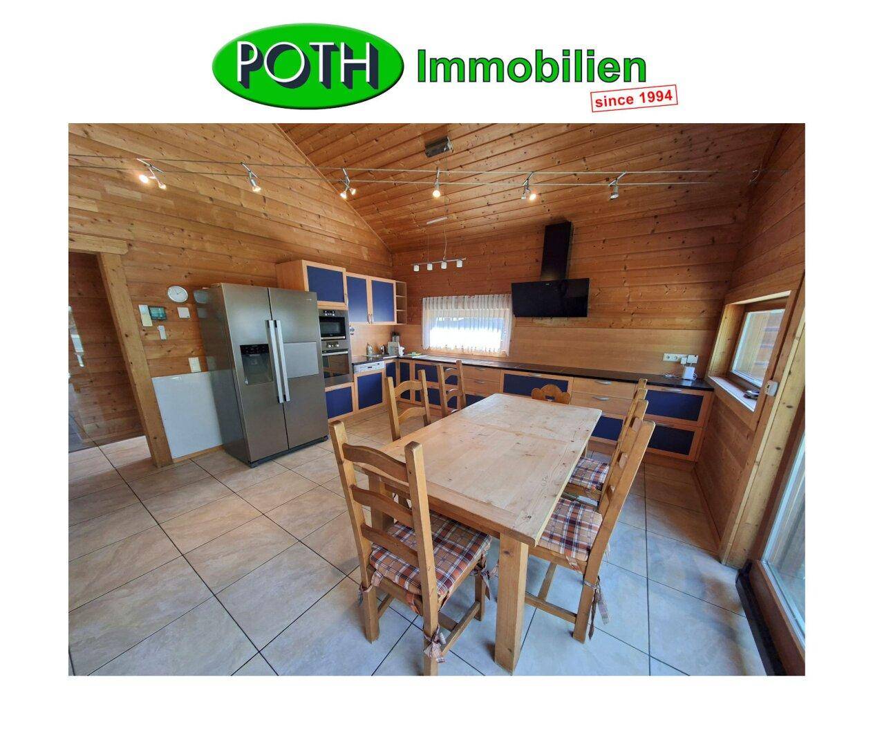 Geräumige Wohnküche mit Holzwänden, blauen Küchenschränken und einem großen Esstisch.