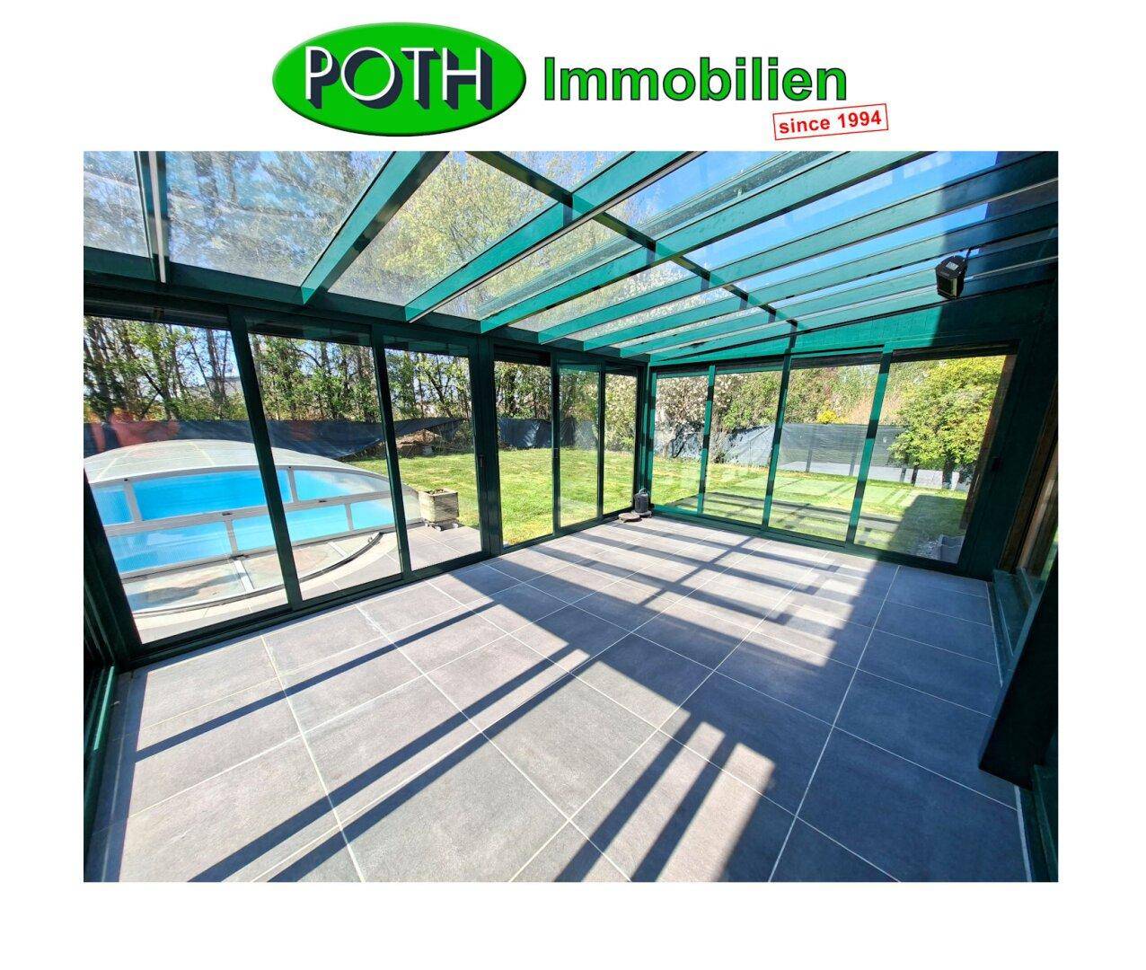 Geräumiger Wintergarten mit großen Fenstern, Fliesenboden und Blick auf den Pool.
