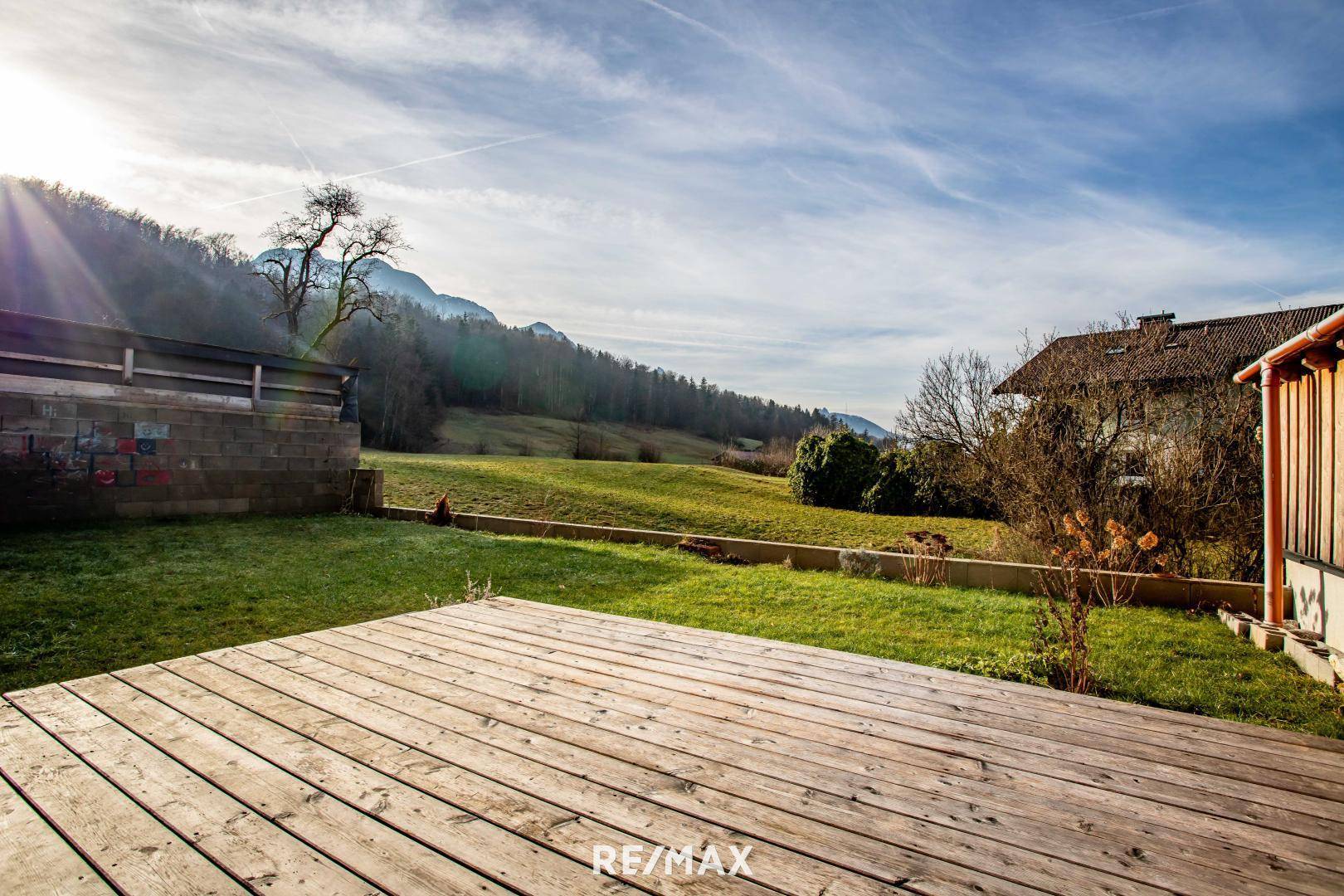 Sonnige Holzterrasse im grünen Garten mit weitem Blick auf die Hügellandschaft.