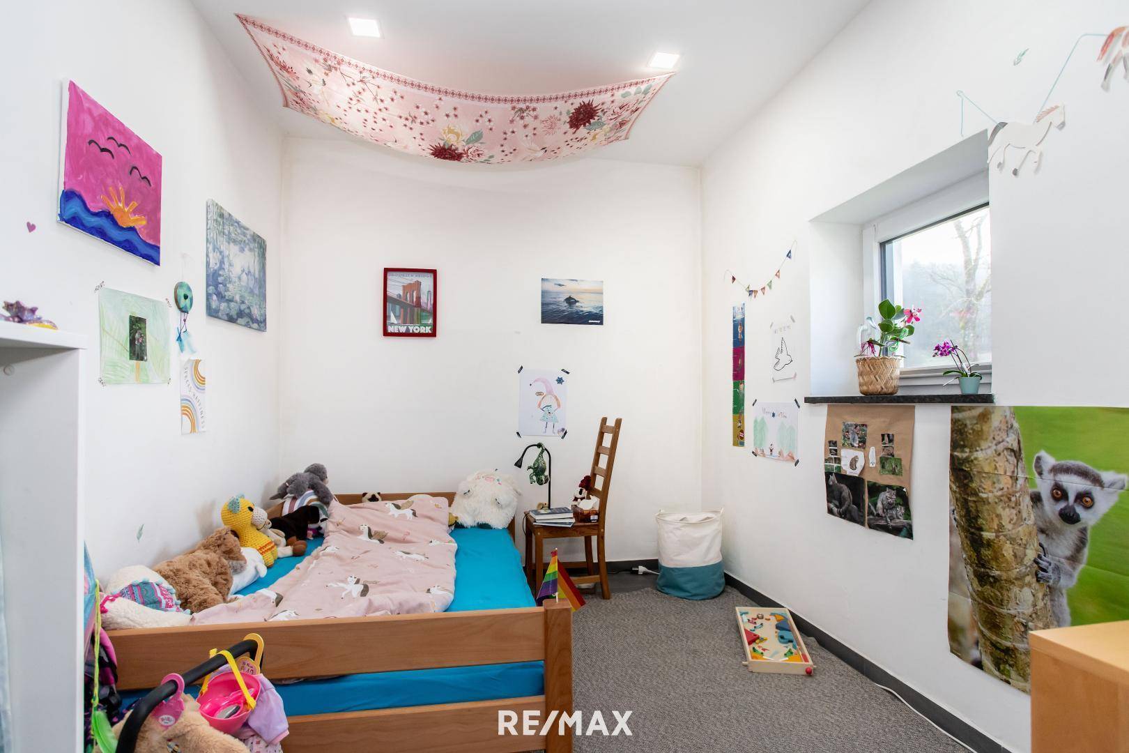 Gemütliches Kinderzimmer mit Holzbett, Fenster und farbenfroher Dekoration.