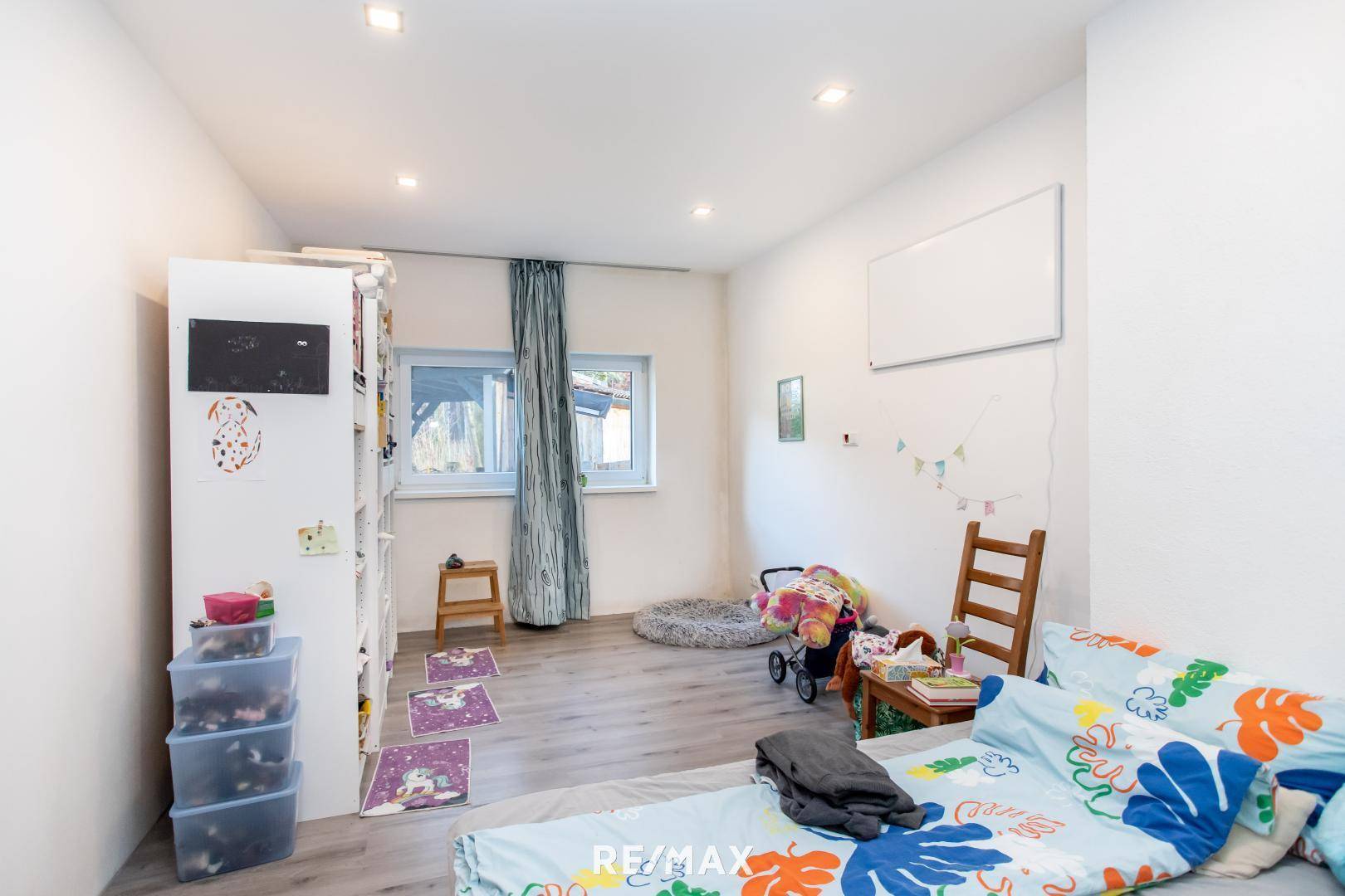 Helles Kinderzimmer mit Laminatboden, weißen Wänden und zwei Fenstern.