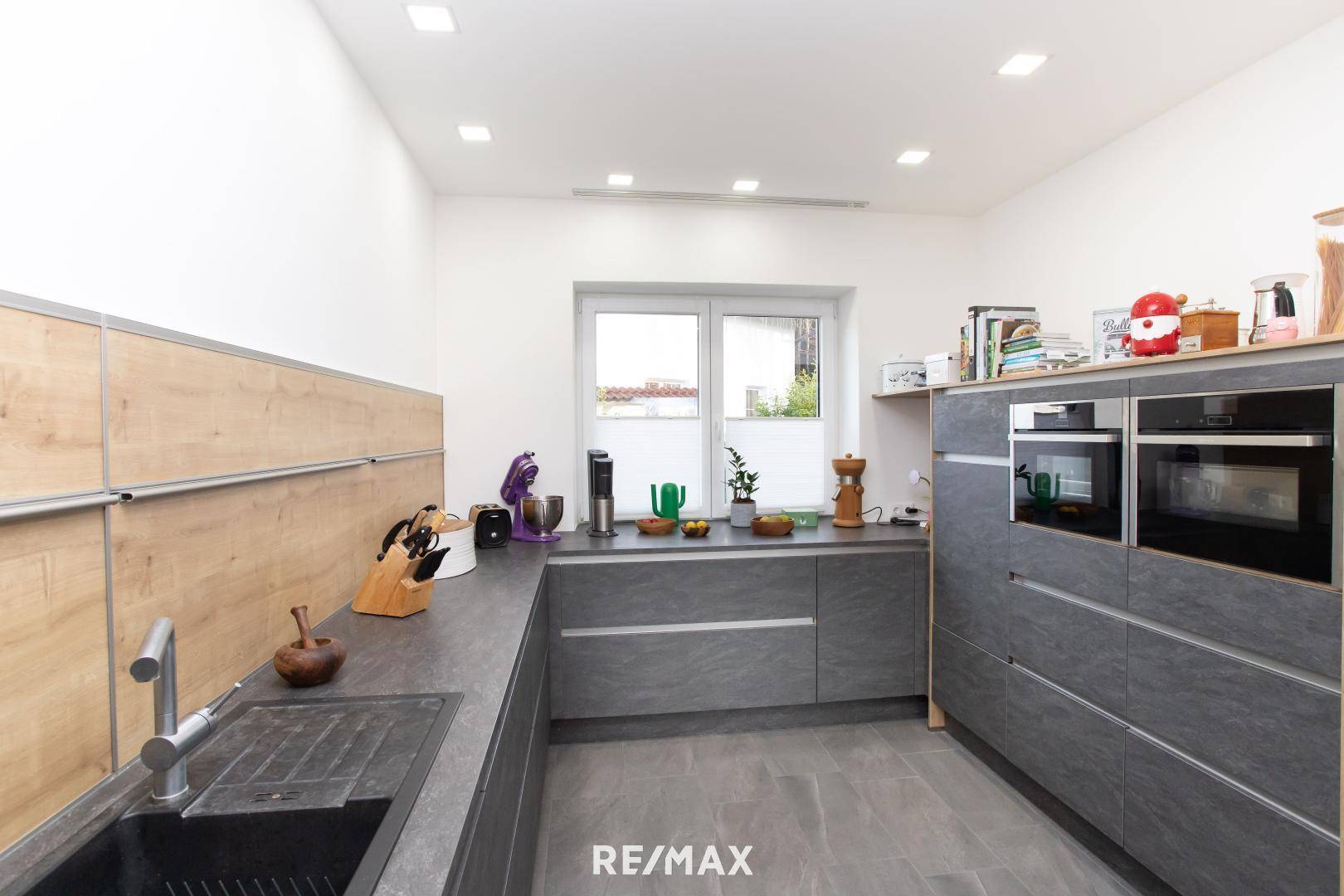 Funktionale Küche mit integrierten Backöfen, Spüle und Fenster für natürliches Licht.