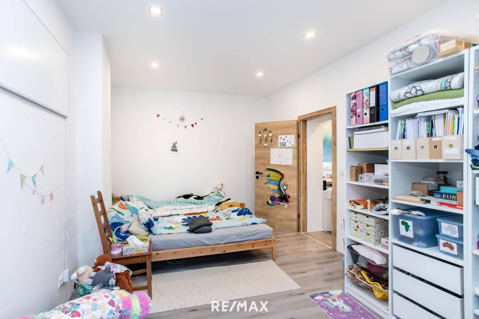 Freundliches Kinderzimmer mit Holzbett, Bücherregal und verspielter Dekoration.