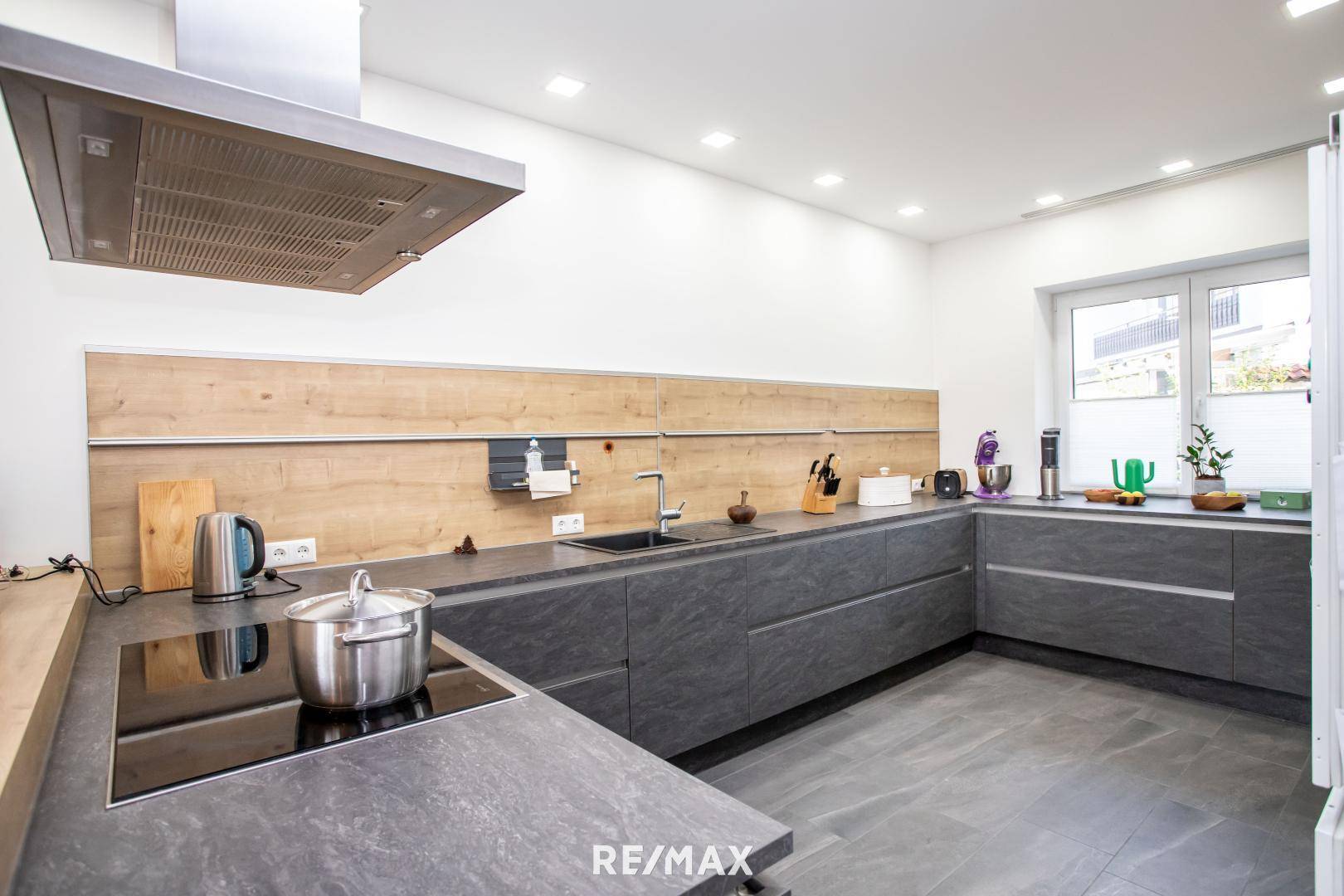 Moderne Einbauküche mit grauen Fronten, Induktionskochfeld und Holzrückwand.