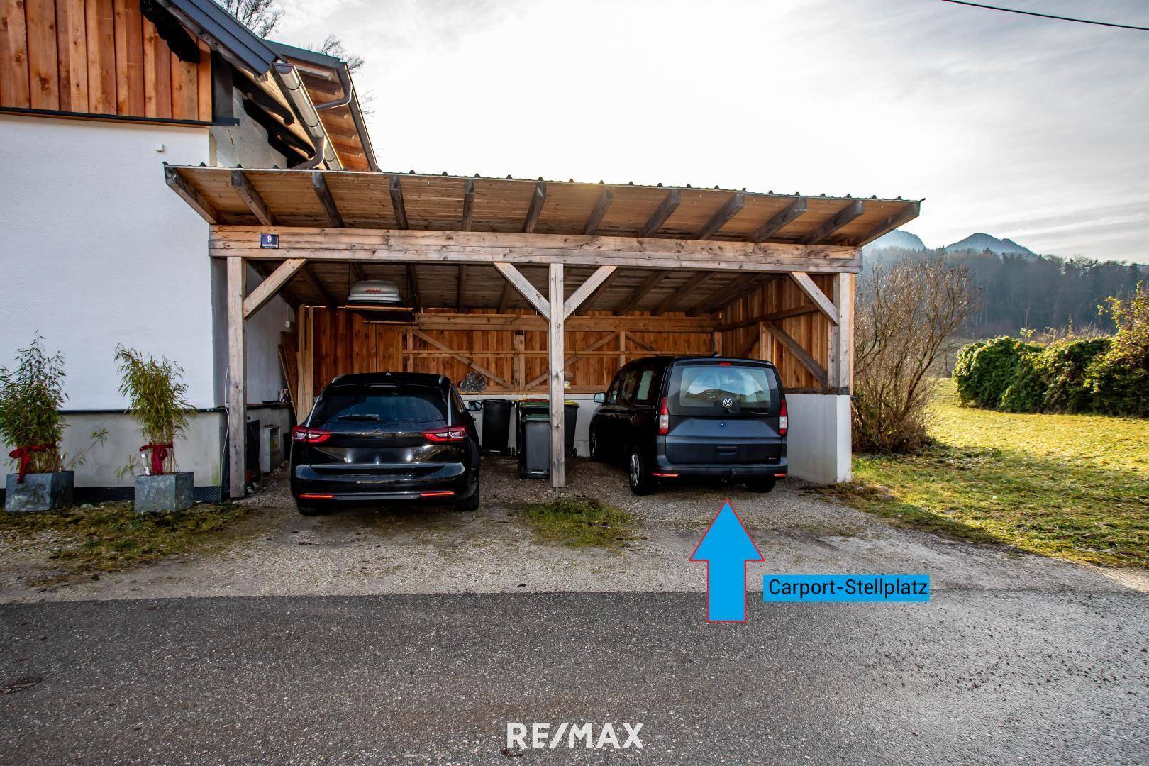 Holzcarport mit zwei Stellplätzen für Fahrzeuge, umgeben von Grünflächen.
