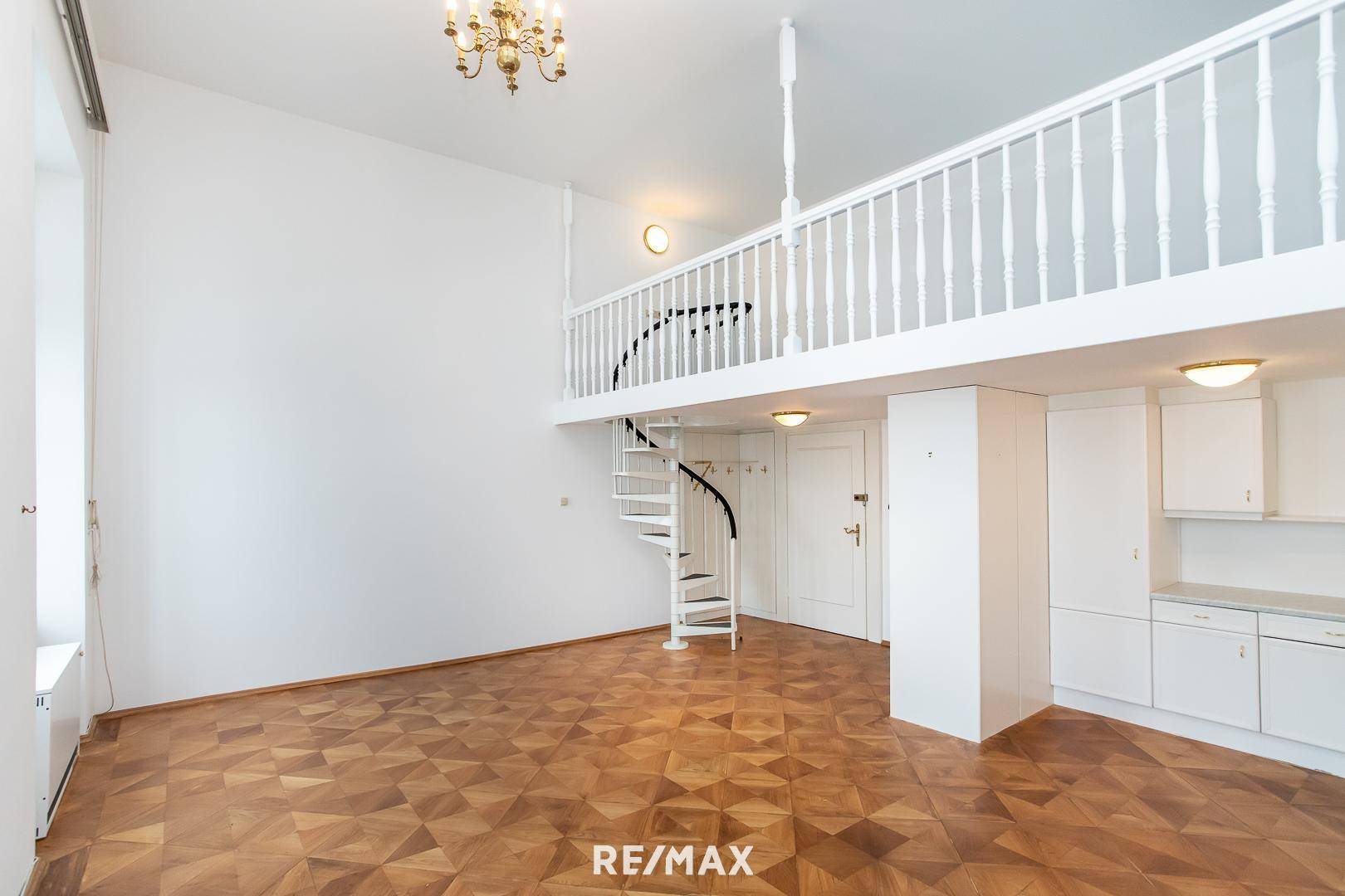 Geräumiger Wohnbereich mit hohen Decken, Wendeltreppe zur Galerie und kleiner Küchenzeile.