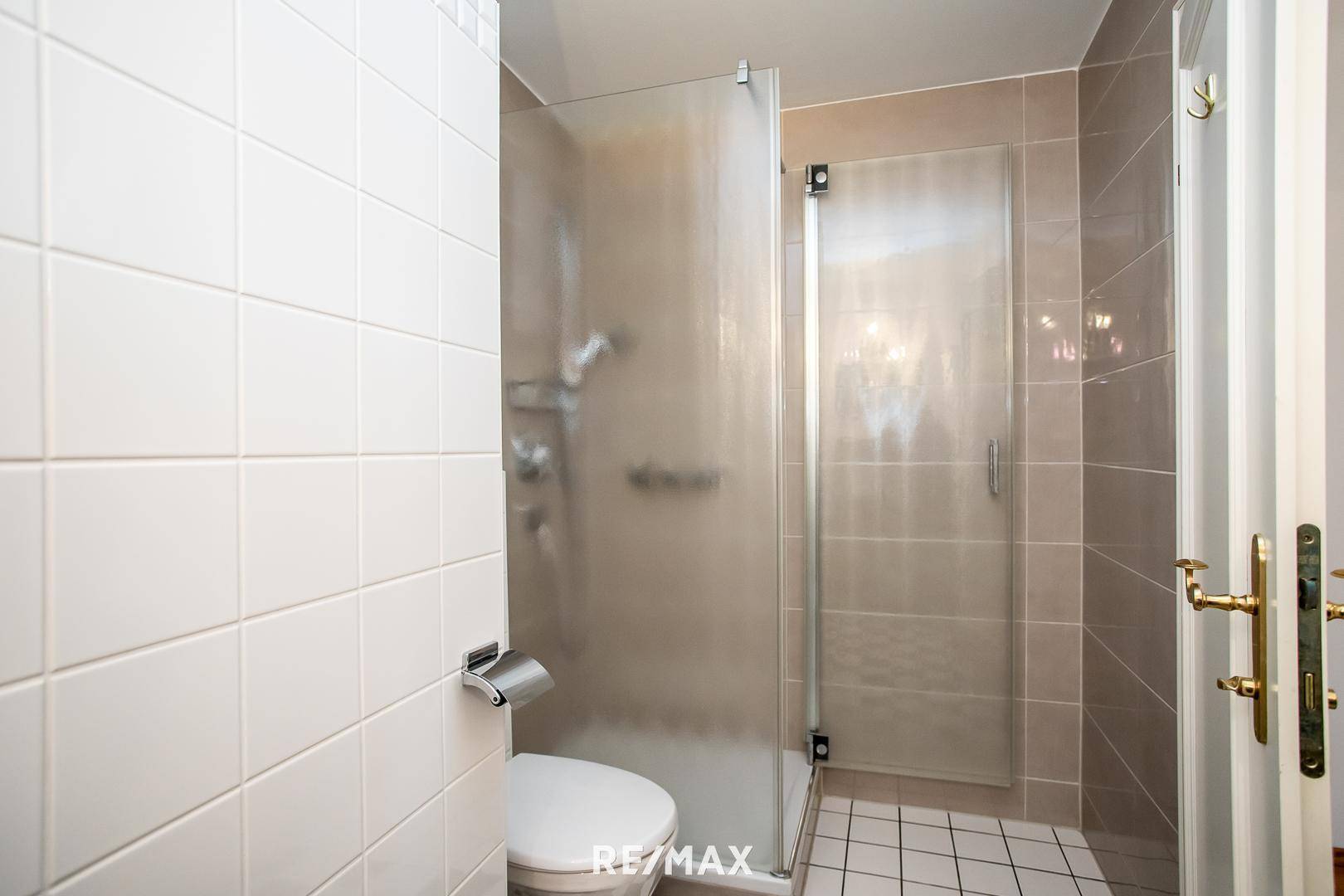 Modernes Badezimmer mit Duschkabine, WC und hellen Fliesen.