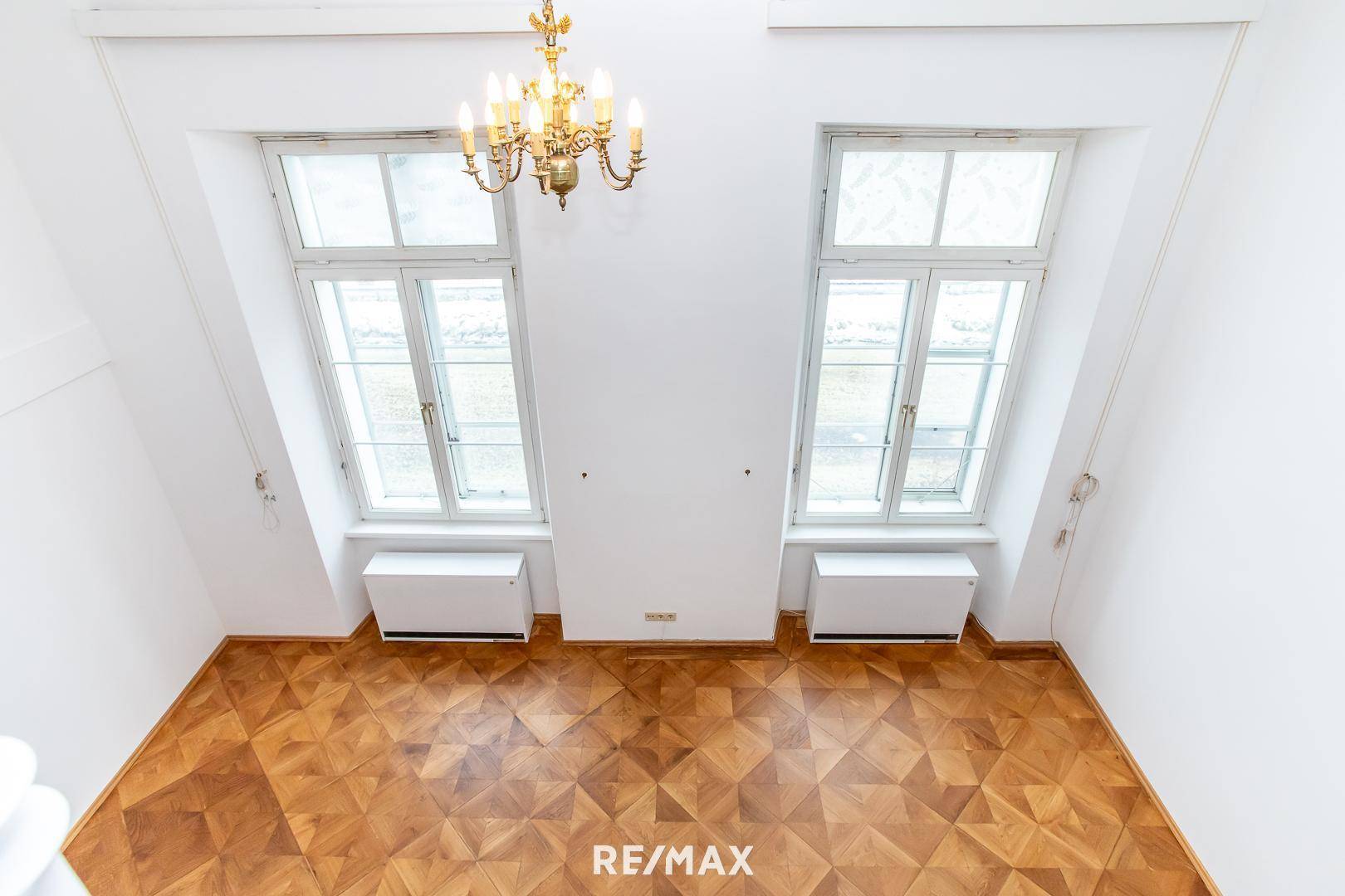 Blick von der Galerie auf den unteren Wohnbereich mit hohen Fenstern und Parkettboden.