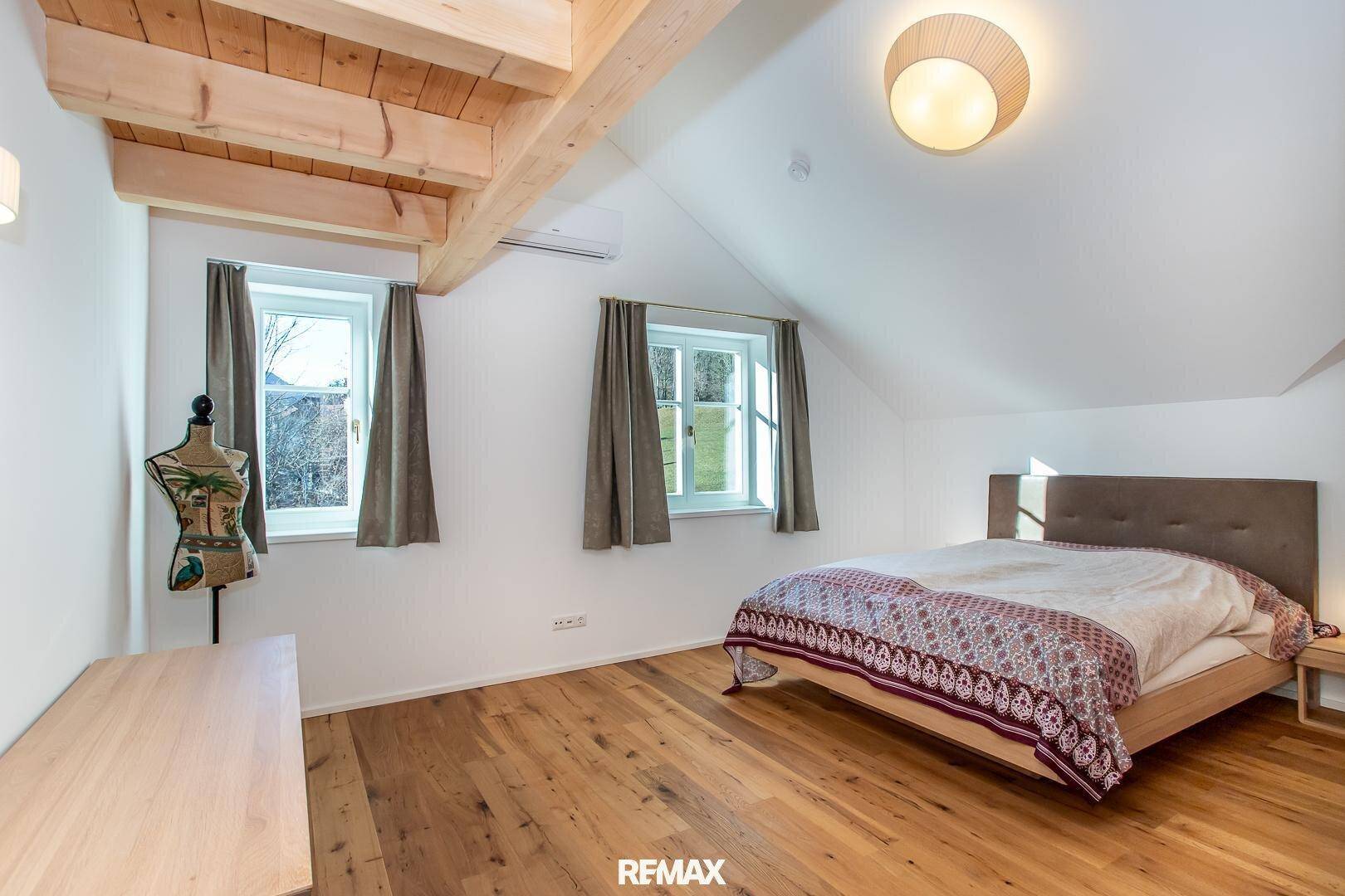 Gemütliches Schlafzimmer mit Holzboden, Dachschrägen und zwei Fenstern für viel Tageslicht.