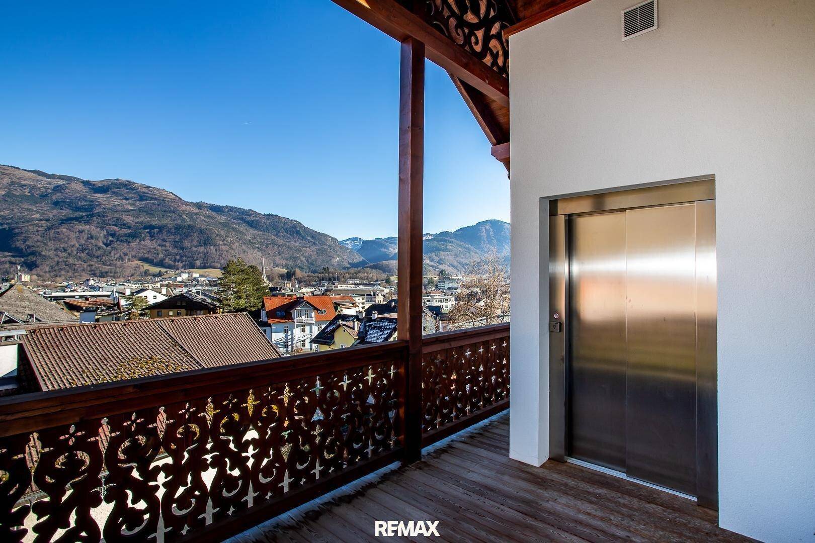 Großer Holzbalkon mit kunstvollen Geländern, Aufzug und weitem Blick auf die Stadt und Berge.