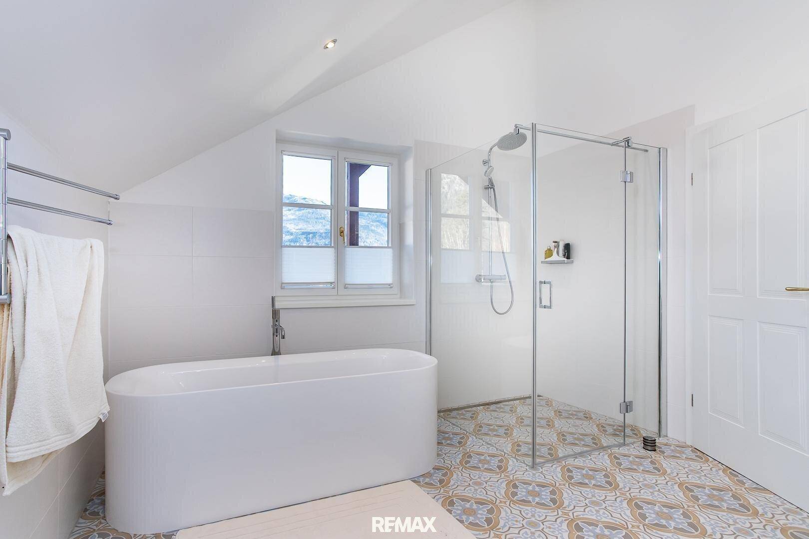 Helles Badezimmer mit freistehender Badewanne, Glasdusche und Fenster mit Bergblick.