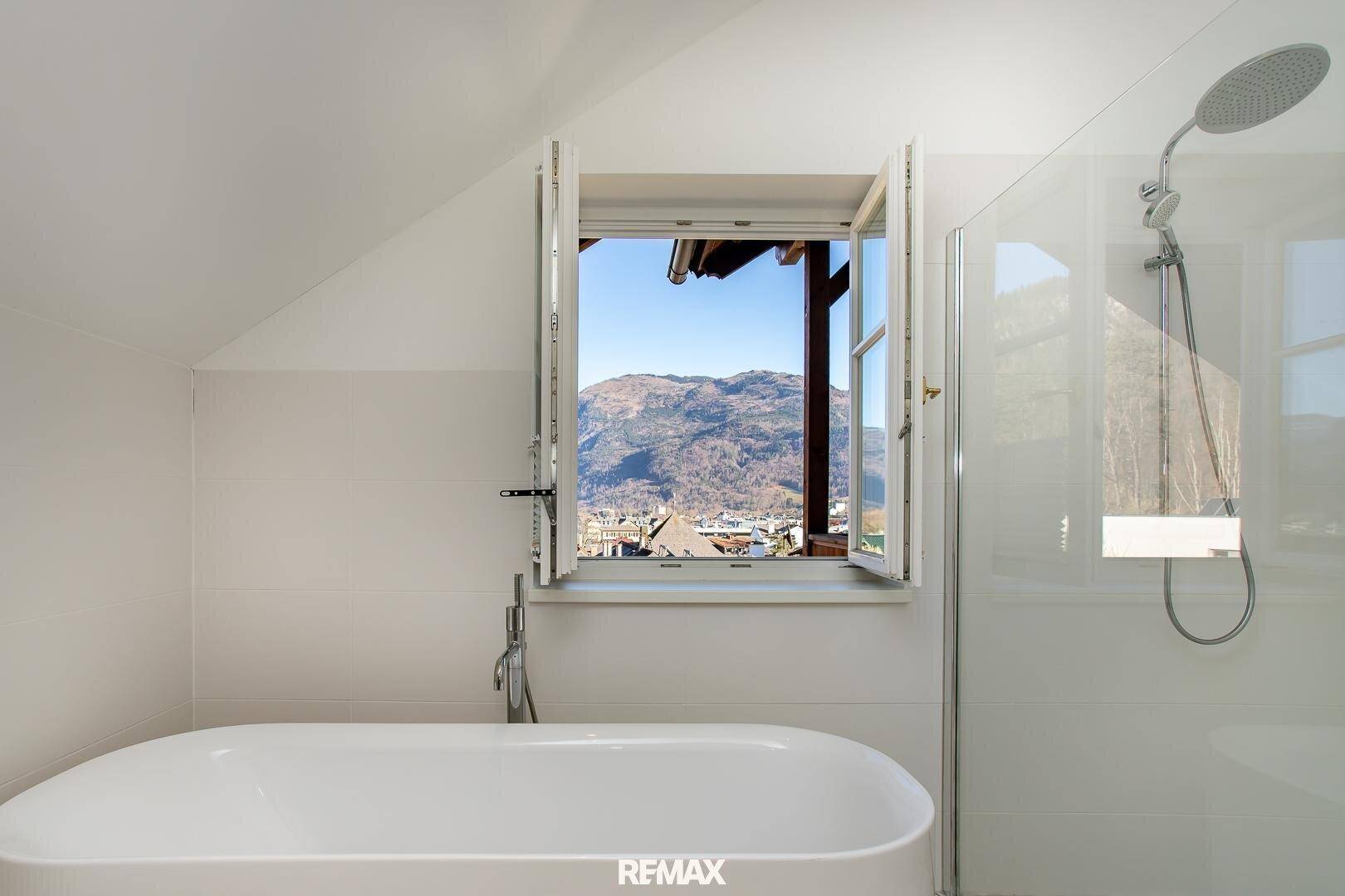 Badezimmer mit freistehender Badewanne und Fenster, das einen weiten Blick auf die Berge bietet.