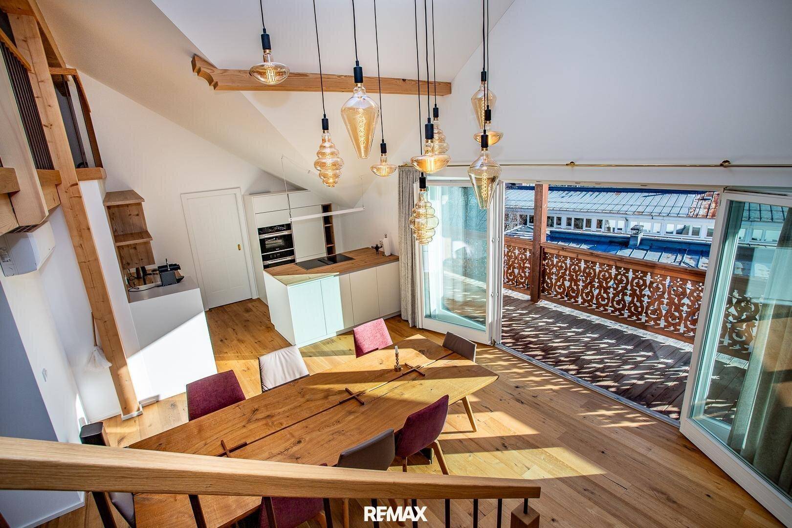 Offener Wohn- und Essbereich mit integrierter Küche, Holzboden und Zugang zu einem großen Balkon.
