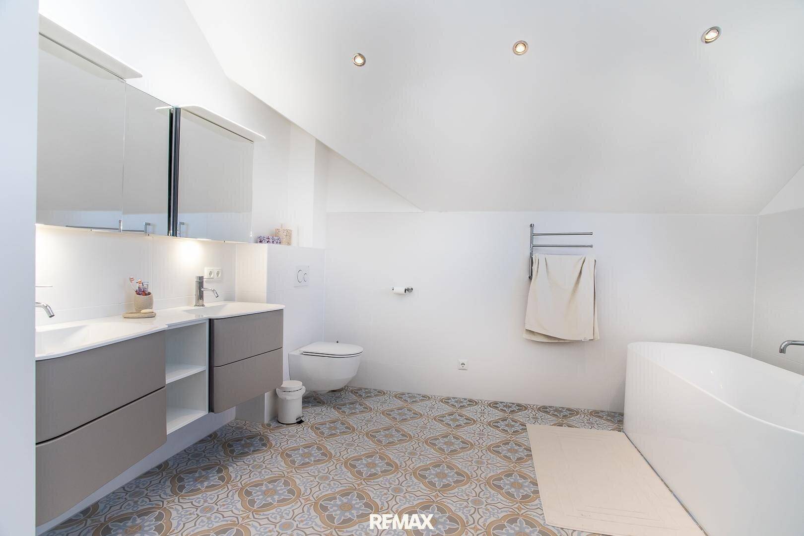 Modernes Badezimmer mit Doppelwaschbecken, freistehender Badewanne und gemusterten Fliesen.