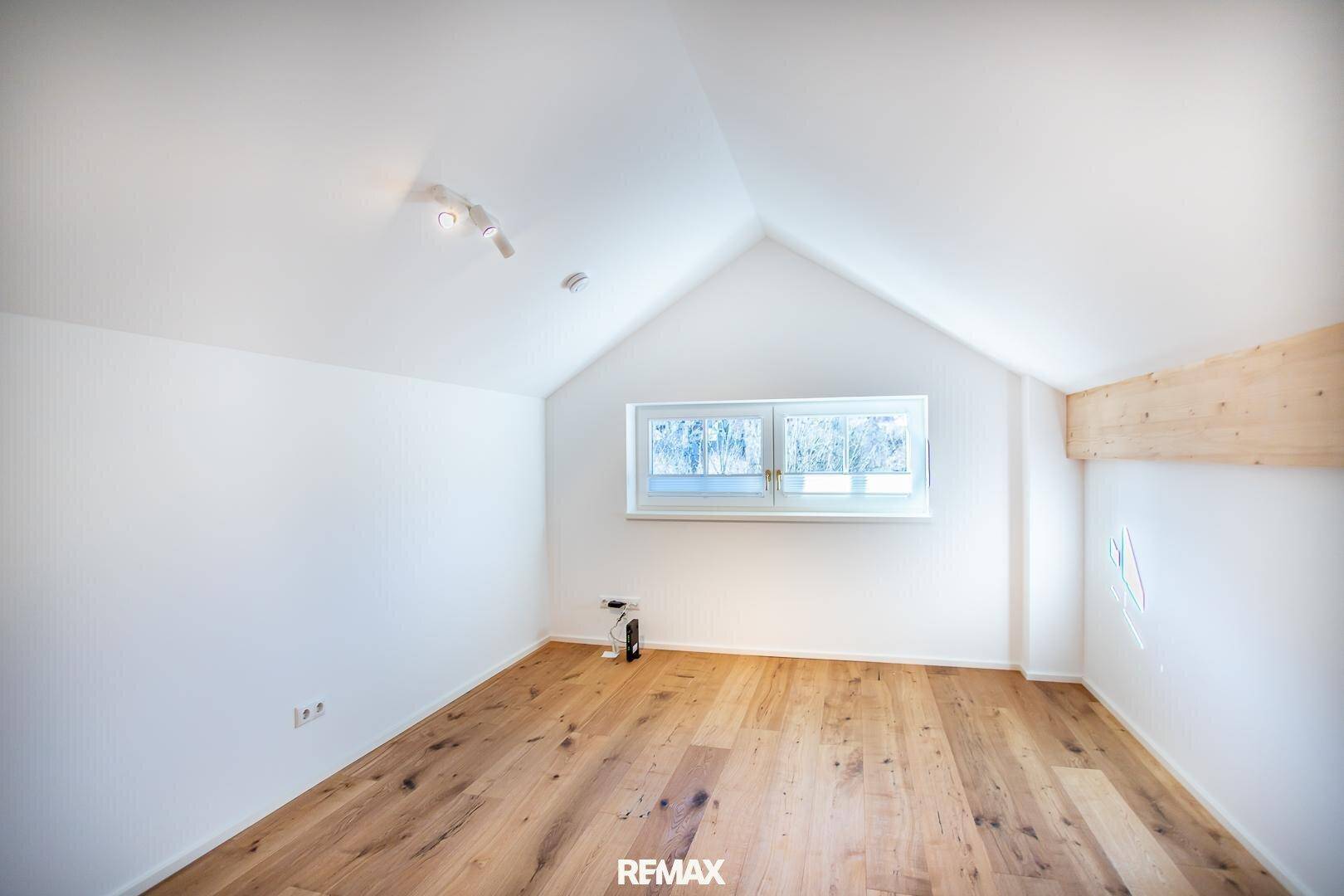 Leeres Zimmer mit Holzboden, Dachschrägen und einem Fenster, bereit zur individuellen Gestaltung.