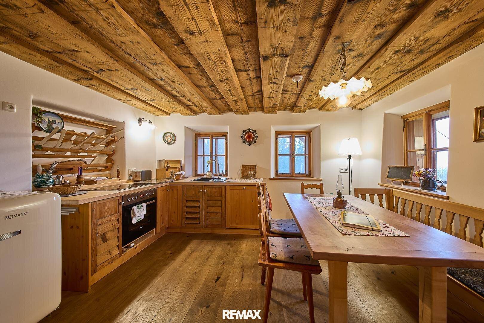 Rustikale Wohnküche mit Holzeinbauten, Holzbalkendecke und Essbereich am Fenster.