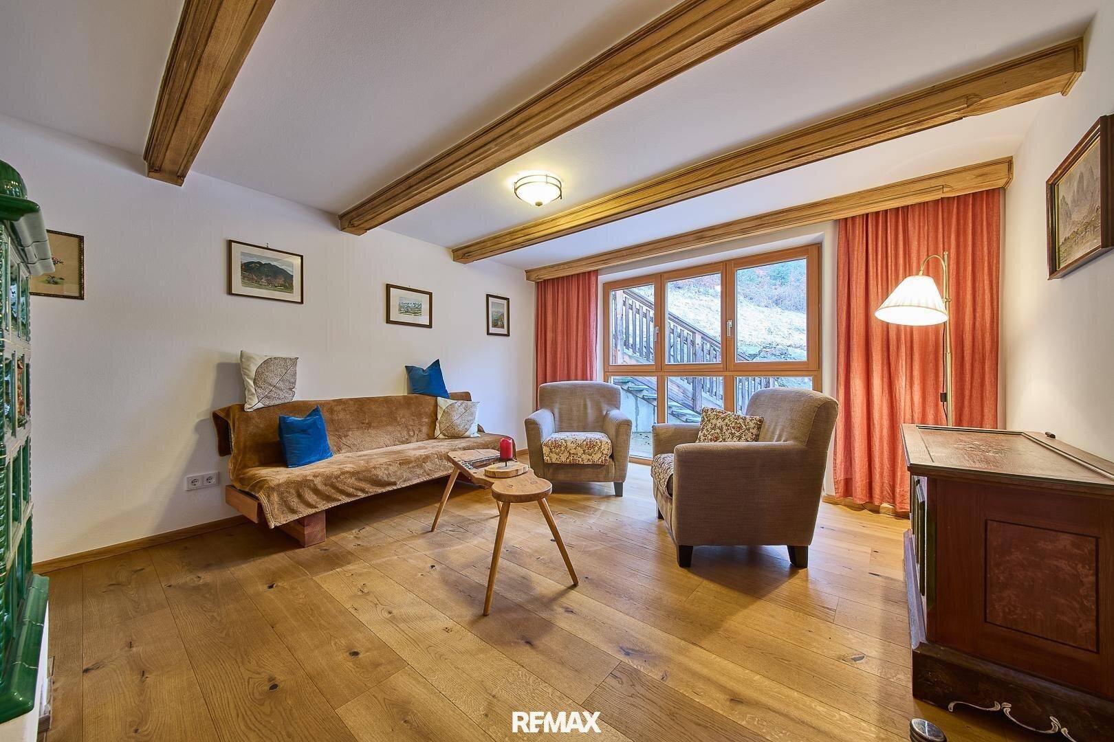 Gemütliches Wohnzimmer mit Holzbalkendecke, Holzboden und einem traditionellen Kachelofen.
